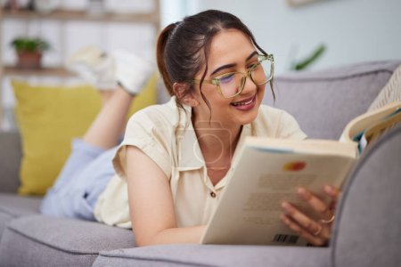Photo for Woman, sofa and reading book in living room for story, novel and learning knowledge. Happy female student, gen z girl and relax with books in lounge for studying, literature or hobby to enjoy at home. - Royalty Free Image