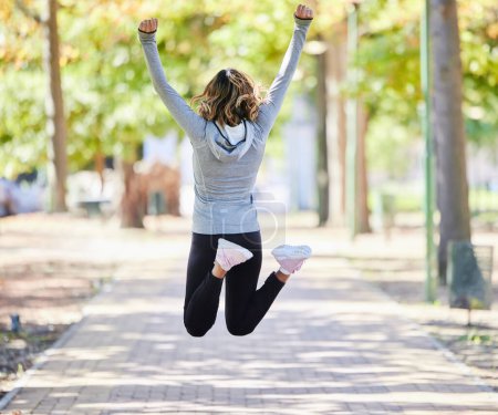 Foto de Fitness, salto y una mujer al aire libre para el éxito en un parque para celebrar la victoria o el logro. Atrás de una joven mujer en un camino en la naturaleza entusiasmada con los objetivos de entrenamiento, correr o entrenar o la libertad. - Imagen libre de derechos