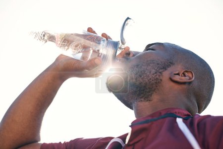 Téléchargez les photos : Homme noir, eau potable et santé avec fitness, athlète et sport avec hydratation et soleil. Homme africain, boisson en bouteille et bien-être avec exercice, fusée éclairante et angle bas. - en image libre de droit
