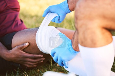 Photo for Bandage, knee pain and injury, medic help athlete and sports accident on field with health and wellness. People outdoor, paramedic dressing wound and medical care with inflammation and fracture. - Royalty Free Image