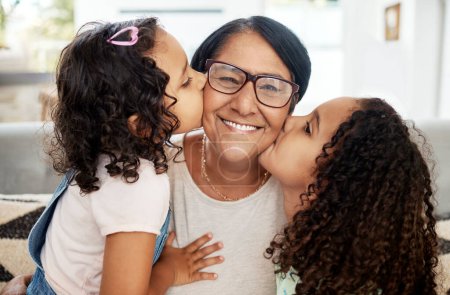 Téléchargez les photos : Les enfants embrassent leur grand-mère sur sa joue avec amour, soin et bonheur dans le salon. Happy, sourire et portrait de la femme âgée étreignant ses filles enfants dans le salon de la maison familiale - en image libre de droit