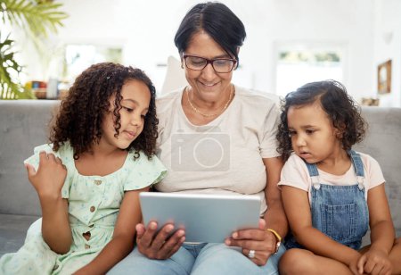 Photo for Tablet, bonding and grandmother watching with children enjoying a video or movie together in the living room. Happy, smile and kids streaming a show on digital technology with a senior woman at home - Royalty Free Image