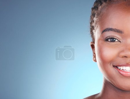 Téléchargez les photos : Portrait de femme noire avec espace maquette pour les soins de la peau, la beauté et le sourire sur fond bleu. Spa esthétique, dermatologie et demi-visage de la personne en studio avec cosmétiques, maquillage et lueur pour le bien-être. - en image libre de droit