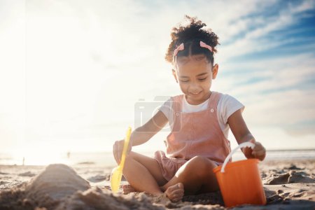 Photo for Sand, castle and girl kid at beach for fun games, freedom and summer holiday with mockup sky. Happy child, bucket and building with play toys at sea for development, vacation and relax in sunshine. - Royalty Free Image