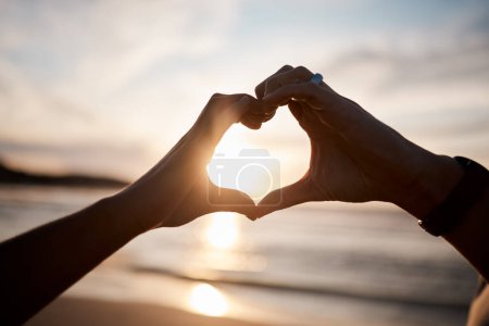Photo for Couple, heart and hands at beach in sunset for love, care and relax on holiday, vacation and travel. Closeup of people, silhouette and finger shape at sea for support, freedom and emoji sign in sky. - Royalty Free Image