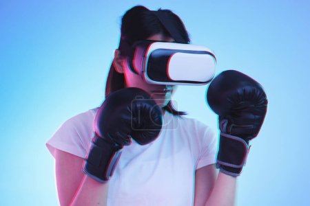 Photo for AI, metaverse and a sports woman boxing on a blue background in studio for fitness or exercise. Virtual reality, gamer and training with a young female boxer playing an online fantasy game for health. - Royalty Free Image