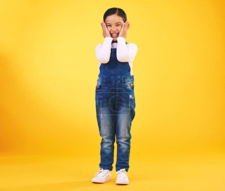 Photo for Excited, happy and hands on face of girl child in studio with news, sale or fashion giveaway on yellow background. Wow, emoji and kid winner with celebration gesture for coming soon surprise prize. - Royalty Free Image