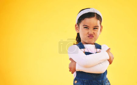 Photo for Arms crossed, portrait and angry girl child in studio with bad, attitude or behavior problem on yellow background. Frown, face and asian kid with body language for no, frustrated or tantrum emoji. - Royalty Free Image