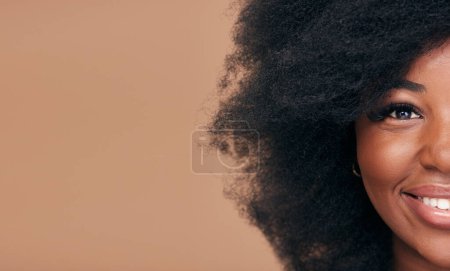 Téléchargez les photos : Portrait, cheveux et maquettes avec un mannequin femme noire en studio sur fond marron pour cosmétiques naturels. Demi-visage, sourire et soins capillaires avec une femme afro heureuse sur l'espace pour le traitement du shampooing. - en image libre de droit