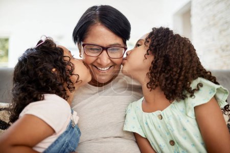 Photo for Kids kissing their grandmother on the cheek with care, love and happiness while relaxing in the living room. Smile, happy and senior woman hugging girl children for bonding together at family home - Royalty Free Image