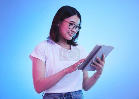 Photo for Young woman, student and tablet for online education, e learning and study on blue, studio background. Happy person typing on digital technology, reading social media and school or youth information. - Royalty Free Image
