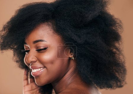 Téléchargez les photos : Beauté, visage et cheveux avec un mannequin femme noire en studio sur fond marron pour les cosmétiques naturels. Sourire, maquillage et soins capillaires avec une jeune femme afro heureuse à l'intérieur pour le traitement du shampooing. - en image libre de droit