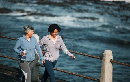 Téléchargez les photos : Fitness, l'exercice et les femmes âgées par l'océan pour le corps sain, le bien-être et le cardio sur la promenade. Sports, amis et femmes avec bouteille d'eau sur la promenade pour la marche, l'entraînement et l'entraînement. - en image libre de droit