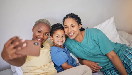 Photo for Gay, happy family and selfie in bed with foster boy child and relax at home. Adoption, lesbian couple and lgbt women on social media, smile for profile picture, blog or post in bedroom on the bed. - Royalty Free Image