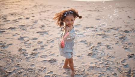 Photo for Girl kid, beach and outdoor with bubbles, playing and freedom with air, games and smile in nature. Young female child, soap and water with plastic toys in wind, summer sunshine and happy on vacation. - Royalty Free Image