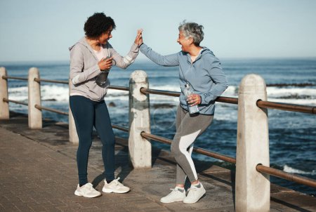 Photo for Fitness, high five and senior women by ocean for healthy lifestyle, wellness and cardio on promenade. Sports, friends and female people celebrate on boardwalk for exercise, training and workout goals. - Royalty Free Image