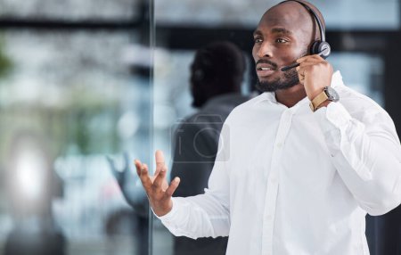 Photo for Black man, microphone and consulting in call center for customer service, advisory help and FAQ questions. Serious salesman working in CRM agency for telecom solution, tech support and communication. - Royalty Free Image