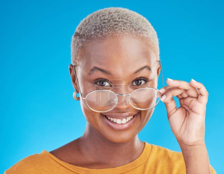 Téléchargez les photos : Happy, portrait et femme noire avec des lunettes sur un fond bleu pour élégant, à la mode et à la mode. Cool, sourire et headshot d'une fille africaine ou d'un modèle d'optométrie avec des lunettes pour la vision et les soins oculaires. - en image libre de droit