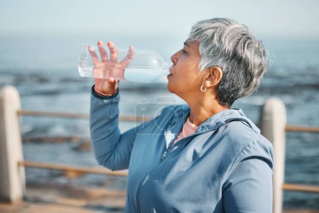 Téléchargez les photos : Extérieur, fitness ou femme âgée boire de l'eau pour l'hydratation, le bien-être et la soif sur la plage, l'entraînement ou l'exercice. Bouteille, coureur ou personne âgée rafraîchir avec du liquide froid lors de l'entraînement à la retraite. - en image libre de droit