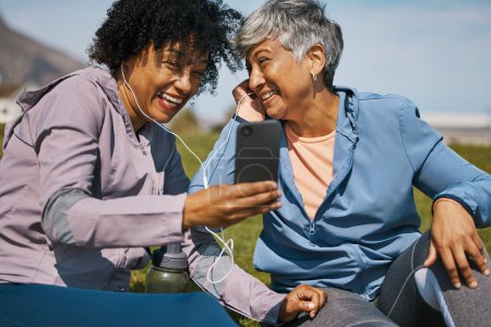Photo for Phone, fitness and music with senior friends on the grass outdoor taking a break from their workout routine. Exercise, smile and elderly people streaming audio while laughing on a field for wellness. - Royalty Free Image