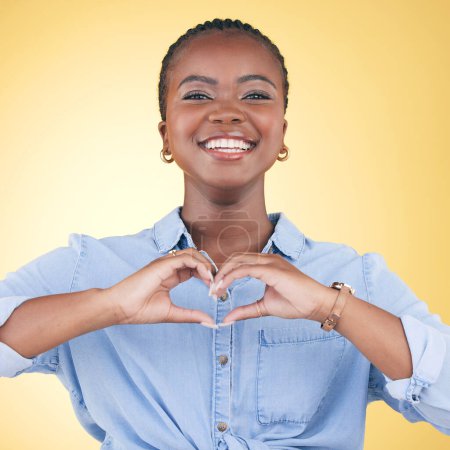 Photo for Happy black woman, portrait and heart hands for love, care or support against a yellow studio background. Face of African female person smile with loving emoji, shape or symbol icon on valentines day. - Royalty Free Image