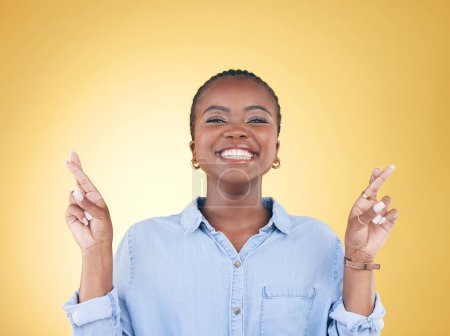 Téléchargez les photos : Signe de vœux, doigts croisés et portrait de femme noire en studio sourire pour l'espoir, la victoire et le succès. Emoji, excité et visage de la personne africaine sur fond jaune avec geste de la main pour le miracle. - en image libre de droit