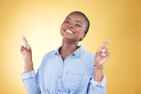 Foto de Mujer africana, dedos cruzados y retrato de estudio para la suerte, sonrisa excitada o ropa de moda de fondo amarillo. Modelo de moda joven, estudiante feliz o lenguaje de signos para la esperanza, el deseo o el sueño de éxito. - Imagen libre de derechos