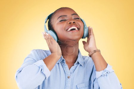 Téléchargez les photos : Femme noire, bonheur et écouteurs avec musique, énergie et streaming audio isolés sur fond jaune. Son, divertissement et radio avec liberté, personne avec plaisir et technologie dans un studio. - en image libre de droit