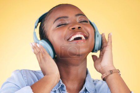 Téléchargez les photos : Chant, musique et femme noire sur casque, heureuse et à l'écoute en studio isolé sur fond jaune. Sourire, radio et personne africaine en streaming podcast, audio et son, ouïe et liberté - en image libre de droit