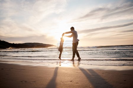 Téléchargez les photos : Amour, balançoire et père avec fille enfant sur une plage tenant la main dans la nature pour le jeu, la liberté ou le lien au coucher du soleil. Océan, voyage et parent avec enfant en mer pour s'amuser, jouer ou célébrer à Bali. - en image libre de droit