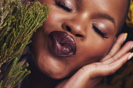 Téléchargez les photos : Femme africaine, plantes et maquillage en studio avec baiser, beauté et bien-être avec rouge à lèvres, peau et gros plan. Fille, modèle et visage avec des feuilles, boudant ou heureux pour les cosmétiques, brillance ou esthétique en zoom. - en image libre de droit