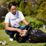 Volunteer, woman and cleaning waste in park for community service, pollution and climate change or earth day project. African person volunteering in garden, nature or outdoor and plastic bag or trash.