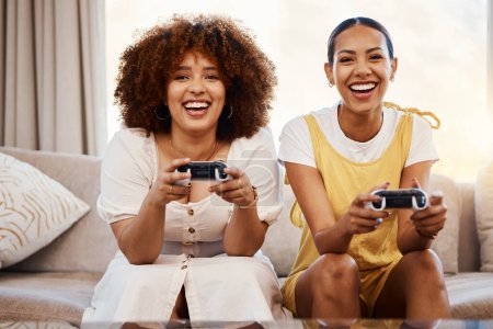 Téléchargez les photos : Les femmes sur le canapé jouer à des jeux vidéo, plaisir excité et se détendre dans le salon à la maison ensemble sur Internet avec contrôleur. Jeux en ligne, esports et amis joueurs heureux sur le canapé avec application virtuelle dans l'appartement. - en image libre de droit