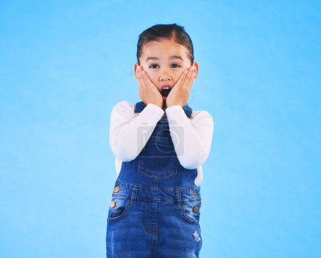 Photo for Portrait, wow and girl excited, surprise and announcement on a blue studio background. Female kid, shock or model with hands on face, emoji and prize with a winner, giveaway or news with mockup space. - Royalty Free Image
