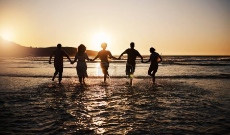 Photo for Water splash, sunset and friends holding hands at a beach with freedom, running or fun vacation rear view. Ocean, silhouette and people shadow in solidarity at the sea for travel, bond or celebration. - Royalty Free Image