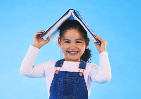 Photo for School, head and portrait of kid with book for knowledge or learning isolated in a studio blue background. Clever, smart and young girl child with notebook happy for education, story or reading. - Royalty Free Image