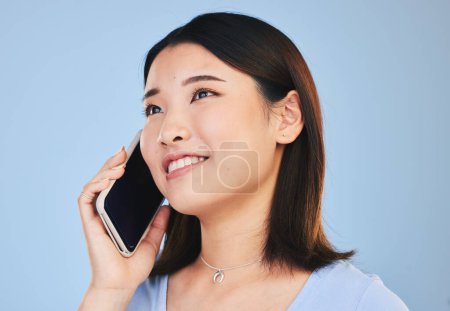 Photo for Asian woman, thinking and phone call in studio with chat, networking and smile by blue background. Young Japanese student, girl and smartphone for contact, mobile connection and memory with ideas. - Royalty Free Image