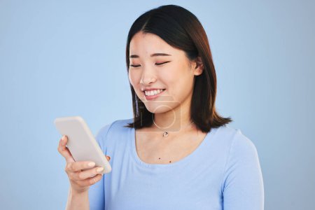 Foto de Mujer asiática feliz, teléfono y mecanografía en las redes sociales, redes o comunicación contra un fondo de estudio azul. Sonrisa de persona femenina en la investigación en línea, chat o mensajes de texto en la aplicación de teléfonos inteligentes móviles. - Imagen libre de derechos