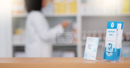 Téléchargez les photos : Mettre l'accent sur une brochure d'information sur un comptoir dans une pharmacie, un traitement publicitaire et des soins de santé avec un pharmacien emballant des rangées de médicaments sur une étagère dans une pharmacie moderne sur fond flou. - en image libre de droit