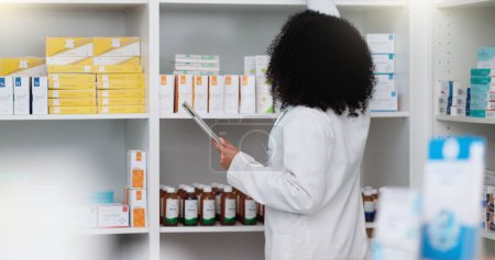 Téléchargez les photos : Young and focused pharmacist use her tablet to do stock taking in a modern pharmacy drugstore. Multiethnic female health professional worker or medication expert in a chemist using a digital gadget. - en image libre de droit