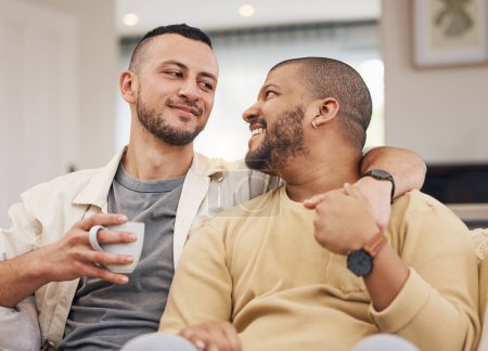 Téléchargez les photos : Couple heureux, amoureux et gay se détendre sur un canapé avec une tasse de café dans le salon ensemble. Sourire, liens et jeunes hommes lgbtq avec un latte assis dans le salon de leur appartement moderne - en image libre de droit