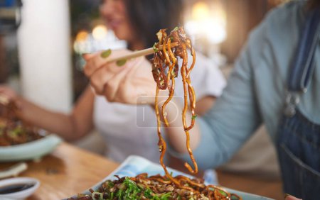 Photo for Food, woman and hand with chopsticks in restaurant eat spaghetti and snack alone at table in closeup bokeh. Supper, person and meal, noodles on plate for lunch or asian dinner for nutrition. - Royalty Free Image