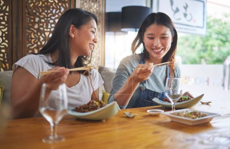 Téléchargez les photos : Restaurant, copines et déjeuner avec de la nourriture, des nouilles et un café heureux de coller. Les femmes asiatiques, manger et assiette avec l'amitié sourire à une table affamée avec des baguettes au bar japonais. - en image libre de droit