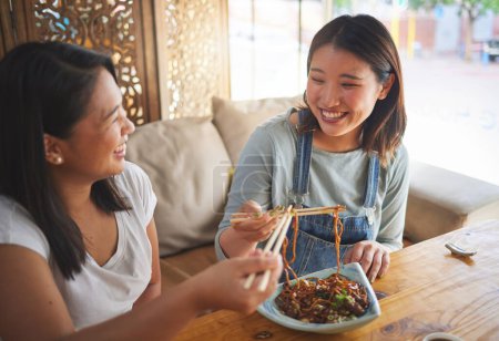 Téléchargez les photos : Baguettes, restaurant et amies mangeant des nouilles et de la cuisine asiatique dans un café. Des femmes heureuses et affamées et une assiette de nourriture dans un bar japonais avec amitié, sourire et coller depuis le repas à une table. - en image libre de droit
