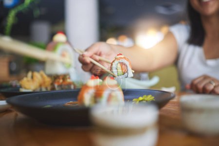 Photo for Chopstick, hand and eating sushi food at restaurant for nutrition at table. Closeup of hungry people with wooden sticks for dining, Japanese culture and cuisine while sharing with creativity on plate. - Royalty Free Image