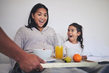 Photo for Surprise, breakfast and mother with child in bed relaxing on weekend morning at their home. Happy, smile and young mom enjoying healthy food for brunch meal with her daughter for mothers day in house. - Royalty Free Image