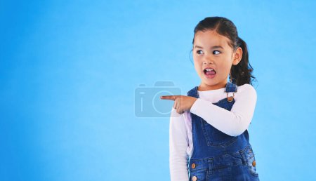 Photo for Pointing, blue background and girl with mockup space for sale, advertising and promotion. Emoji, happy and young child in studio with hand gesture for discount information, announcement and news. - Royalty Free Image