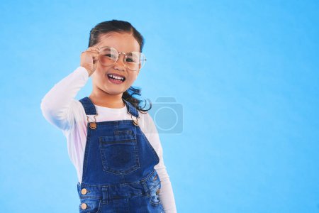 Photo for Girl child, glasses and frame in studio portrait for vision, health and eye care by blue background. Female kid, test spectacles and young fashion model with lens, smile or eyesight with mockup space. - Royalty Free Image