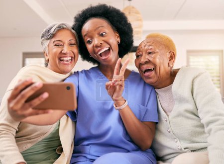 Téléchargez les photos : Selfie, soignant et femmes âgées avec signe de paix pour les médias sociaux, poste en ligne ou photo de profil sur le canapé. Retraite, maison de retraite et infirmière avec des personnes âgées prennent des photos pour des souvenirs heureux. - en image libre de droit
