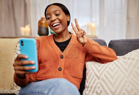 Téléchargez les photos : Selfie, femme noire et signe de paix à la maison avec un sourire pour les médias sociaux, la motivation et parfait. Photo, femme heureuse et africaine dans un salon avec un geste de la main v et emoji à la maison. - en image libre de droit